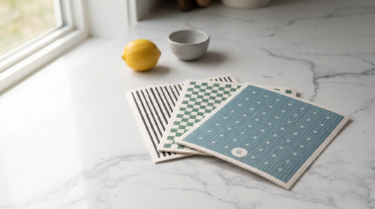 Good Change Eco Cloths - charcoal stripe, sage check and dusty blue designs fanned on a marble kitchen bench in natural light